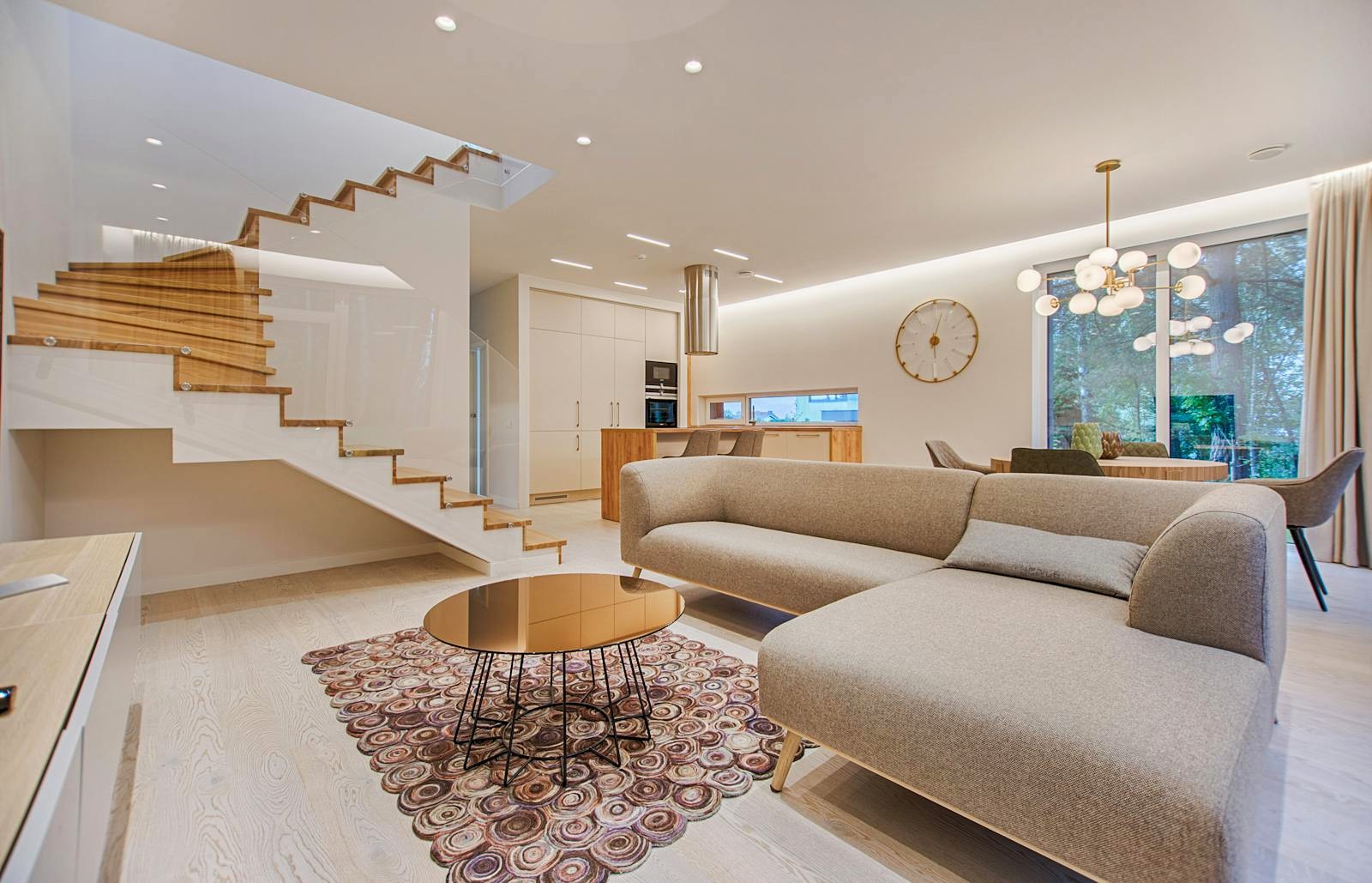 Bright open-plan living room with wooden staircase and window view of trees